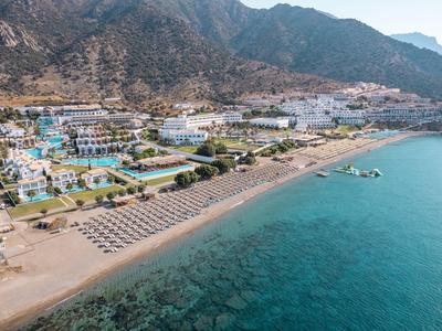 Resort sulla spiaggia con lettini e ombrelloni vicino al mare azzurro e montagne sullo sfondo.