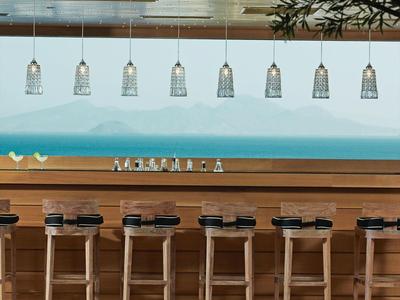 Moderner Hotelbarbereich mit Holztheke, sechs Hockern und dekorativen Hängelampen.