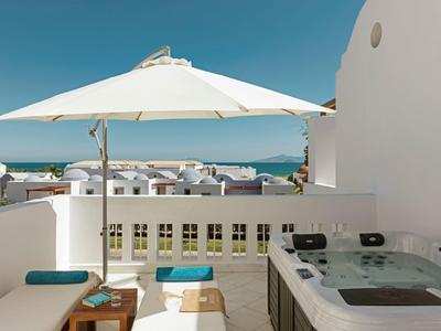 Terrazza con ombrellone bianco, jacuzzi, posti a sedere e vista mare sotto un cielo sereno.