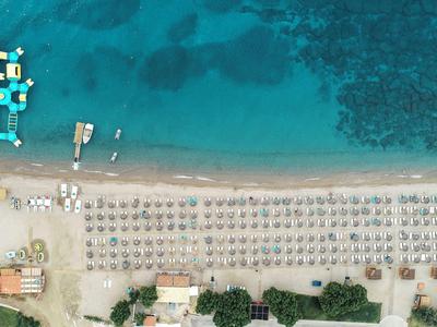 Vista aerea di una spiaggia con lettini, ombrelloni e acqua azzurra limpida con barche vicino alla riva.