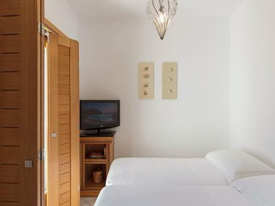 Camera semplice con pareti bianche, letti singoli, mobile TV in legno e decorazioni murali.