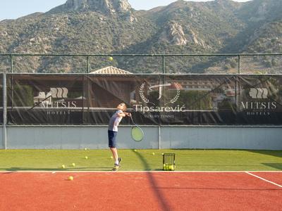 Personne jouant au tennis sur un court rouge avec des montagnes en arrière-plan au soleil.