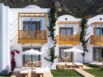 Villas d'hôtel blanches avec balcons en bois, verdure et piscine bleue devant un paysage montagneux.