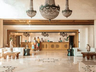 Grande hall d'hôtel avec comptoir, éclairée par des lustres et un sol en marbre luxueux.