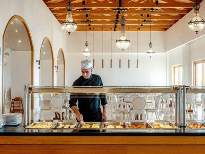 Chef derrière un buffet avec divers plats dans un restaurant lumineux avec plafond en bois.