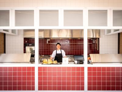 Un chef prépare de la nourriture dans une cuisine ouverte avec des carreaux rouges.