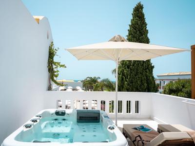 Bain à remous sur terrasse avec chaise longue, parasol et vue sur mer et arbres.