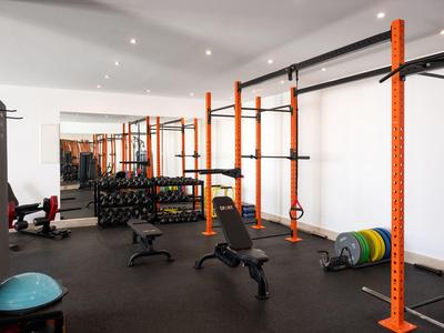 Salle de sport moderne avec poids, bancs et cadres d'entraînement orange le long du mur.