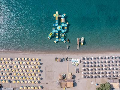 Vue aérienne d'une plage avec parasols et un parc aquatique flottant en mer.