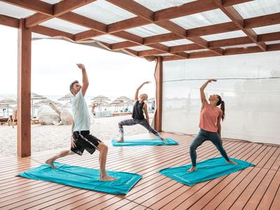 Trois personnes font du yoga sur des tapis bleus sous un pavillon en bois sur une terrasse.