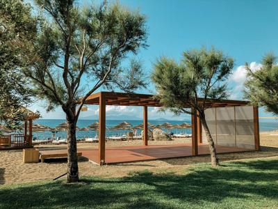 Structure en bois offrant de l'ombre sous les arbres sur la plage avec vue sur des parasols et la mer.