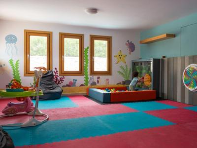 Salle de jeux colorée pour enfants avec mur d'escalade, coussins et grandes fenêtres dans un hôtel.