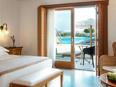 Helles Hotelzimmer mit offenem Balkon und Blick auf einen Pool und das Meer.
