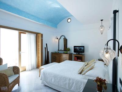 Camera d'hotel luminosa con letto matrimoniale, poltrona, cassettiera, TV e porte balcone.