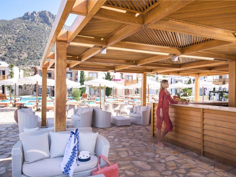 Area bar esterna in legno con sedute e donna in vestito rosso che cammina.