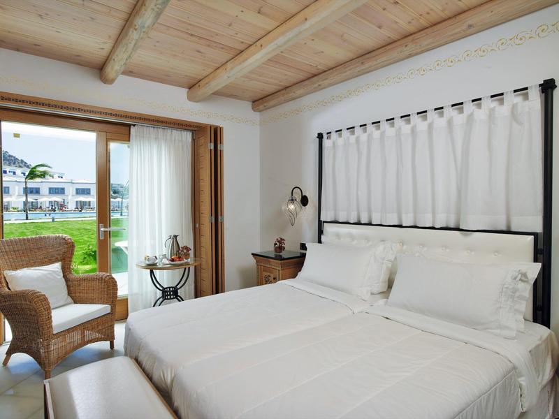 Camera d'hotel luminosa con grande letto, poltrona in vimini, soffitto in legno e vista sul giardino.