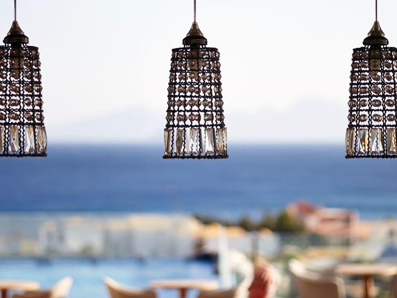 Tre lampade a sospensione in vimini sopra un'area pranzo esterna vicino al mare.