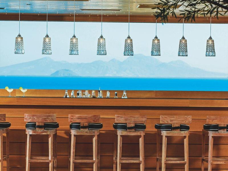 Bar in legno moderno con sgabelli sotto luci sospese e murale di montagna.