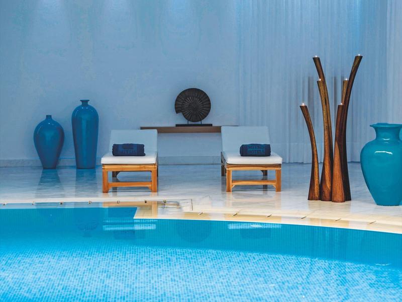 Area piscina moderna con vasi blu, sedie e illuminazione soffusa di sera