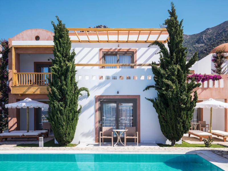 Casa vacanze moderna con piscina, due cipressi alti e montagne sullo sfondo.