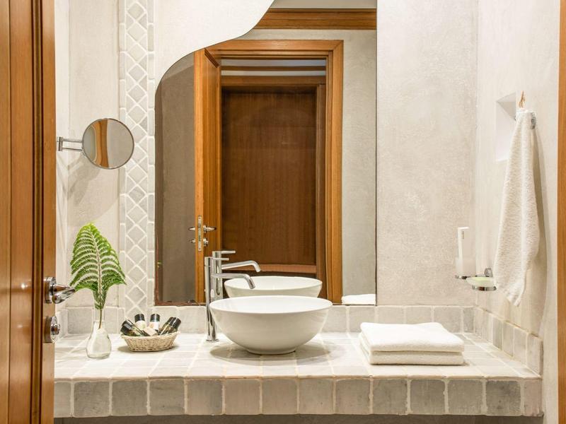 Bagno moderno con grande specchio, lavabo a ciotola, asciugamani e pantofole.