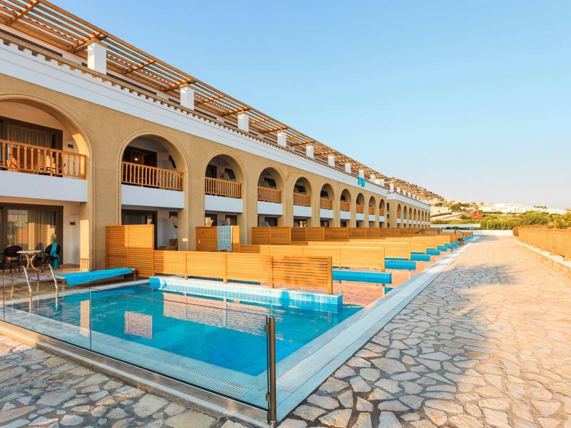 Hotel con piscine private accanto alle camere lungo un vialetto in pietra sotto un cielo limpido.