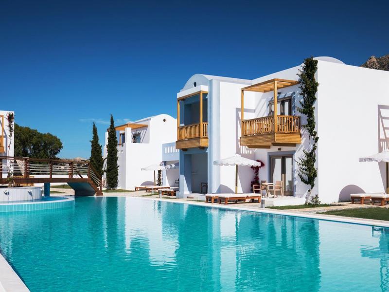 Complesso alberghiero moderno con edifici imbiancati a calce e grande piscina sotto un cielo azzurro.