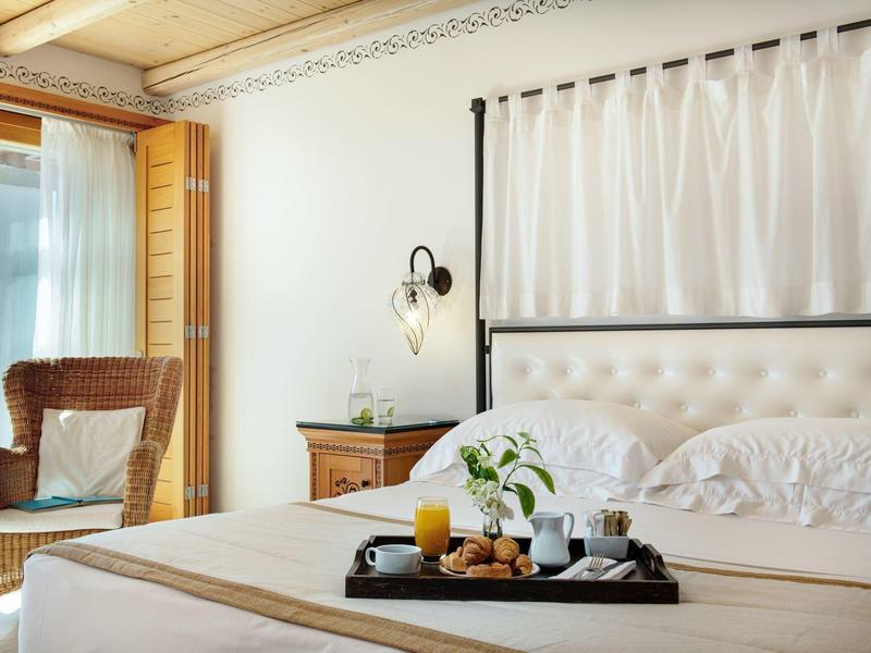 Camera d'hotel accogliente con letto grande, vassoio per la colazione e poltrona vicino al balcone.