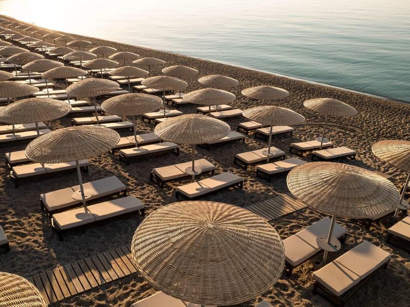 File di ombrelloni e lettini su una spiaggia sabbiosa vicino a acqua calma al tramonto.