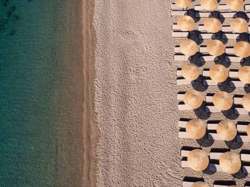 Vista aerea di una spiaggia con file ordinate di ombrelloni e lettini accanto ad acqua blu chiara.