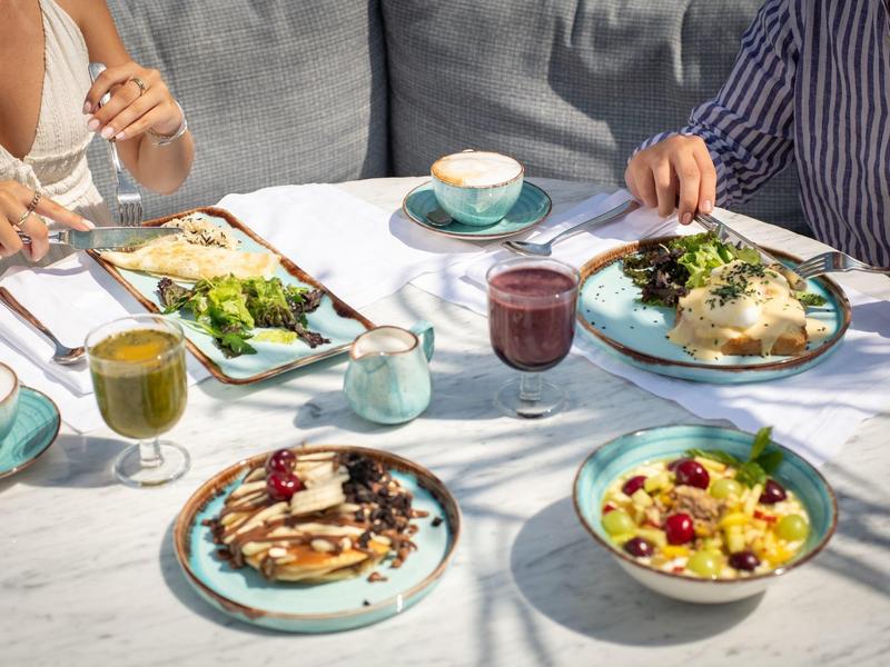 Due persone che pranzano all'aperto con vari piatti colorati e bevande su un tavolo in marmo bianco.