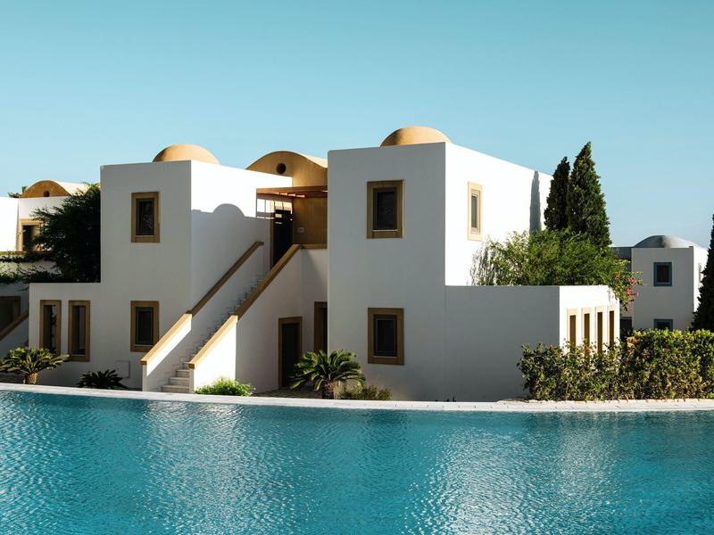 Edificio mediterraneo bianco accanto a una piscina azzurra sotto un cielo limpido.