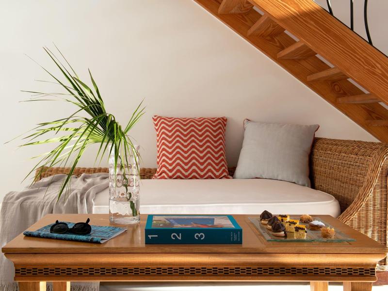 Divano in rattan sotto le scale con cuscini e tavolino in legno con giochi e pianta.
