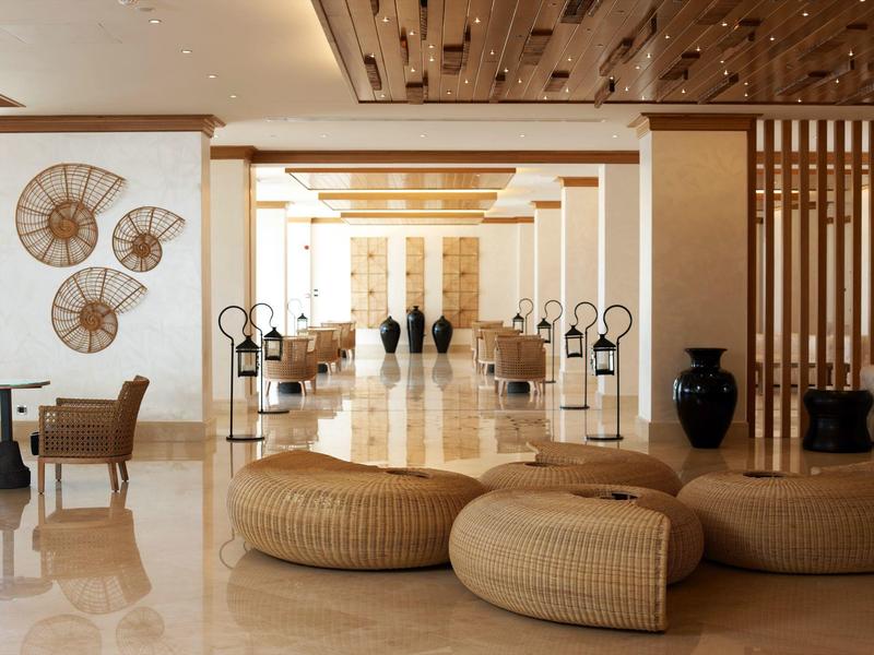 Ampio e moderno atrio d'hotel con pouf beige, dettagli in legno e decorazioni murali artistiche.