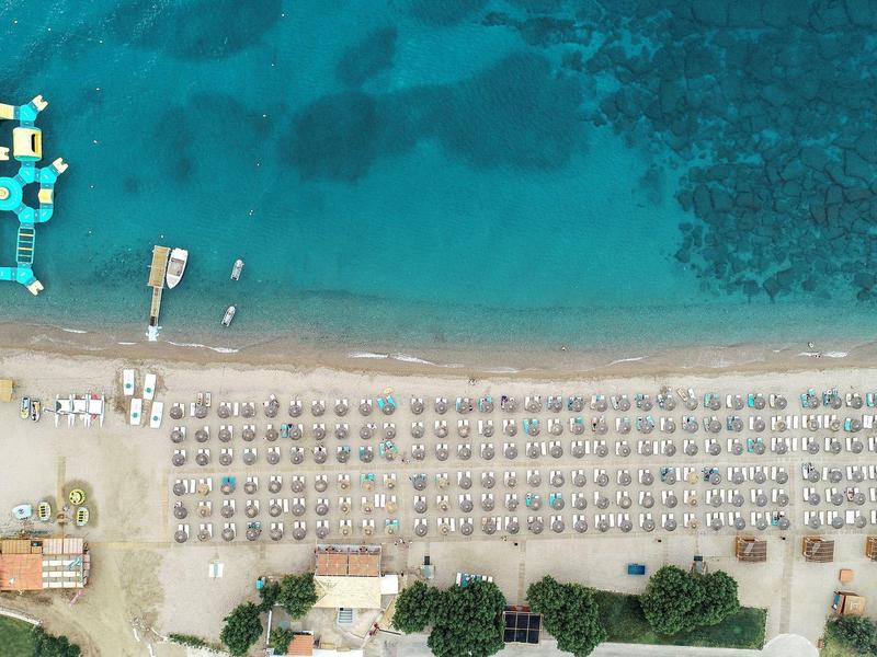 Vista aerea di una spiaggia con lettini, ombrelloni e acqua azzurra limpida con barche vicino alla riva.