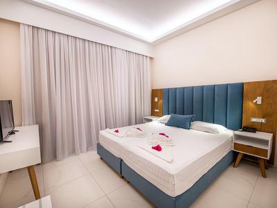 Nowoczesny pokój hotelowy z podwójnym łóżkiem, niebieskim zagłówkiem i białymi meblami.