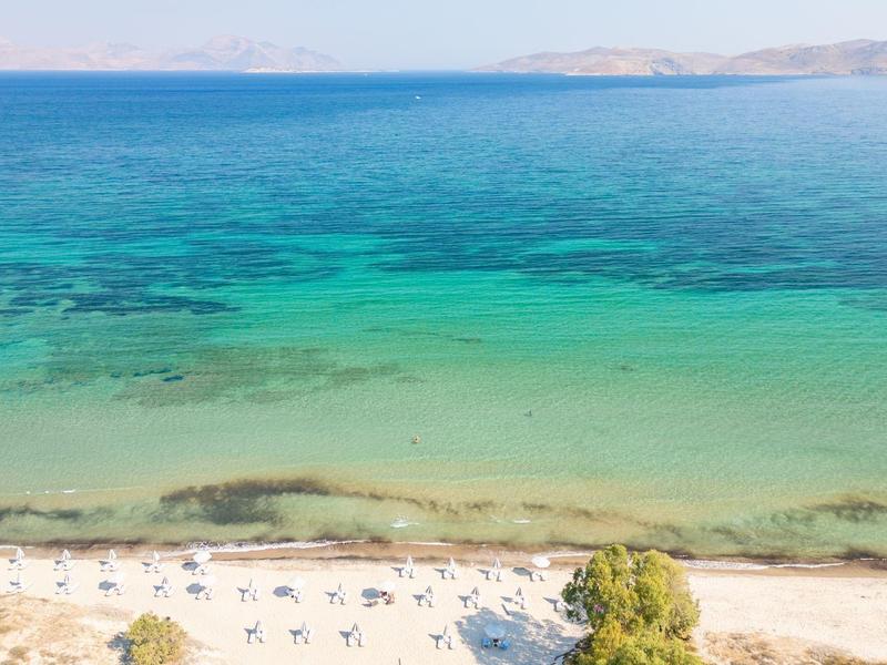 Widok na spokojną plażę z czystą turkusową wodą i leżakami.