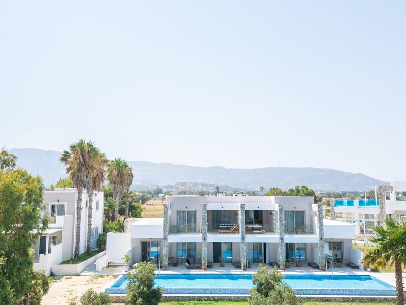 Nowoczesne białe wille z niebieskimi basenami i zielonym krajobrazem na tle gór.