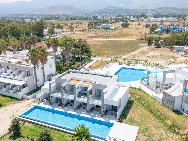 Kompleks hotelowy z kilkoma basenami otoczony zielonym krajobrazem i górami w tle.