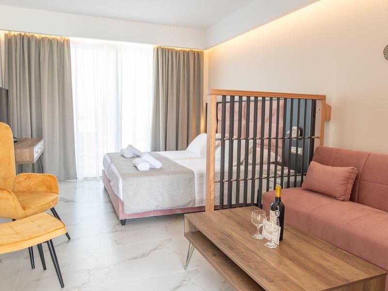 Nowoczesny pokój hotelowy z częścią wypoczynkową, łóżkiem, drzwiami tarasowymi i ciepłymi kolorami.