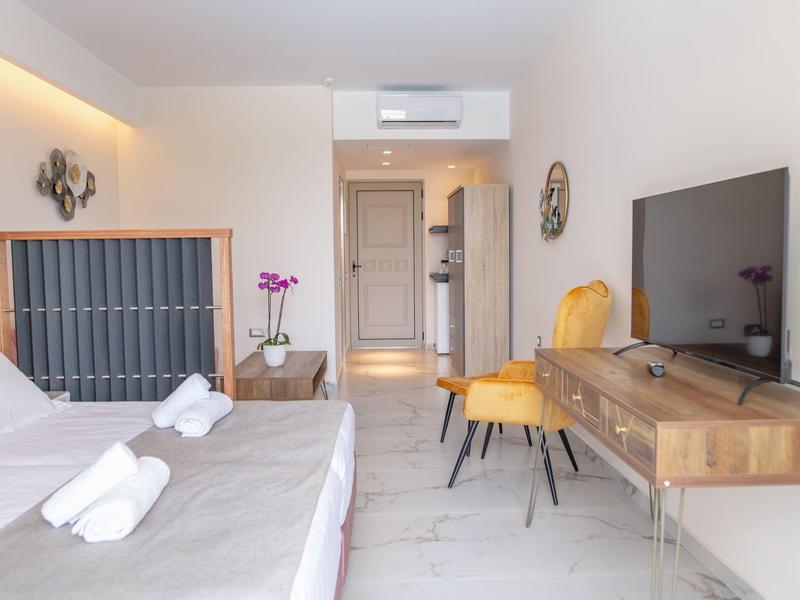 Nowoczesny pokój hotelowy z łóżkiem, telewizorem na drewnianych meblach i dwoma żółtymi krzesłami.