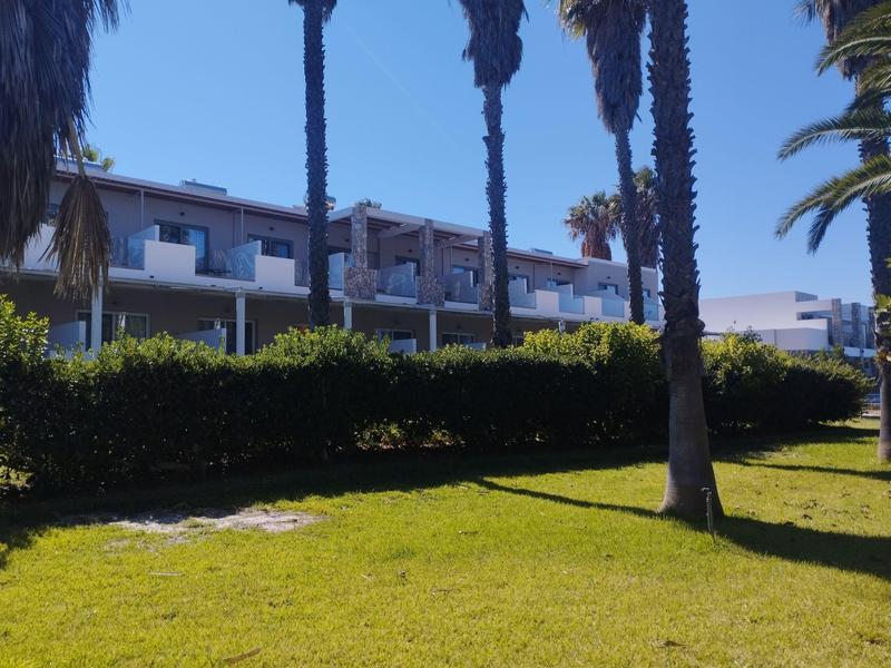 Nowoczesny budynek hotelowy z białymi balkonami i palmami na zadbanym trawniku.