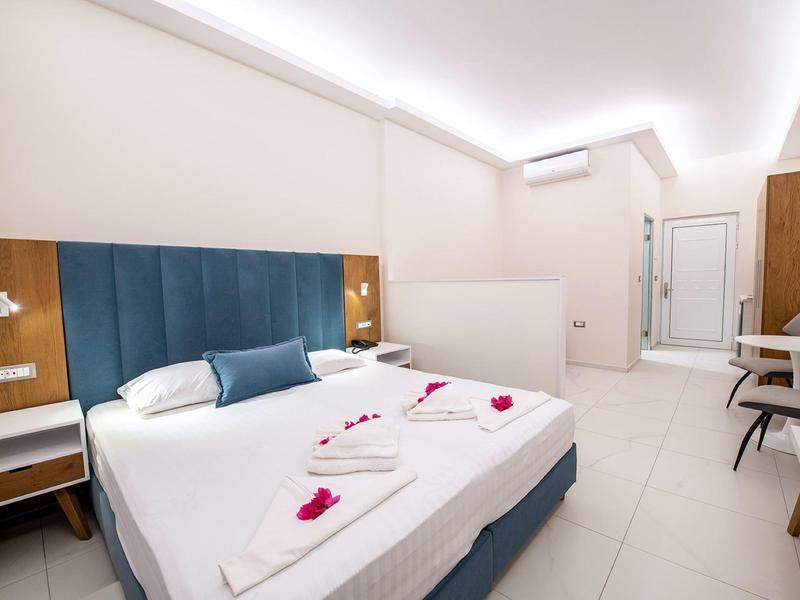 Nowoczesny pokój hotelowy z dużym łóżkiem podwójnym, niebieskim zagłówkiem i prostym wystrojem.