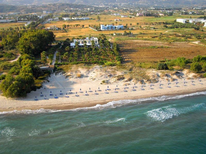 Widok z lotu ptaka na plażę z parasolami i pobliską roślinnością przy spokojnym morzu.