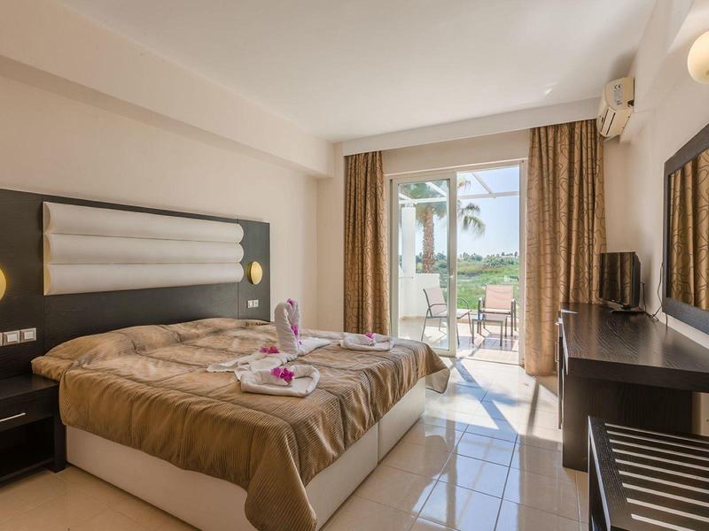 Jasny pokój hotelowy z podwójnym łóżkiem, tarasem i widokiem na palmy.
