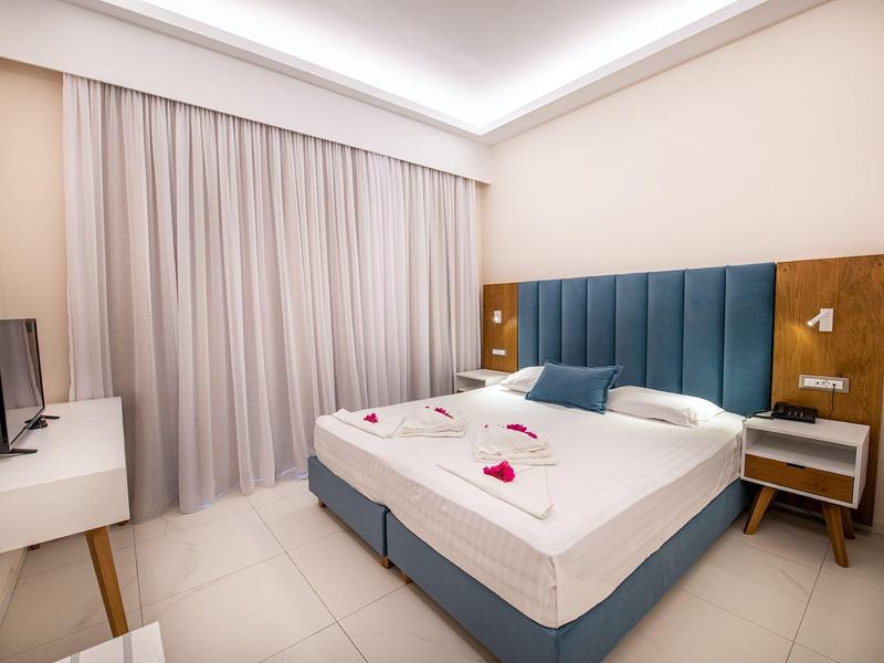 Nowoczesny pokój hotelowy z podwójnym łóżkiem, niebieskim zagłówkiem i białymi meblami.