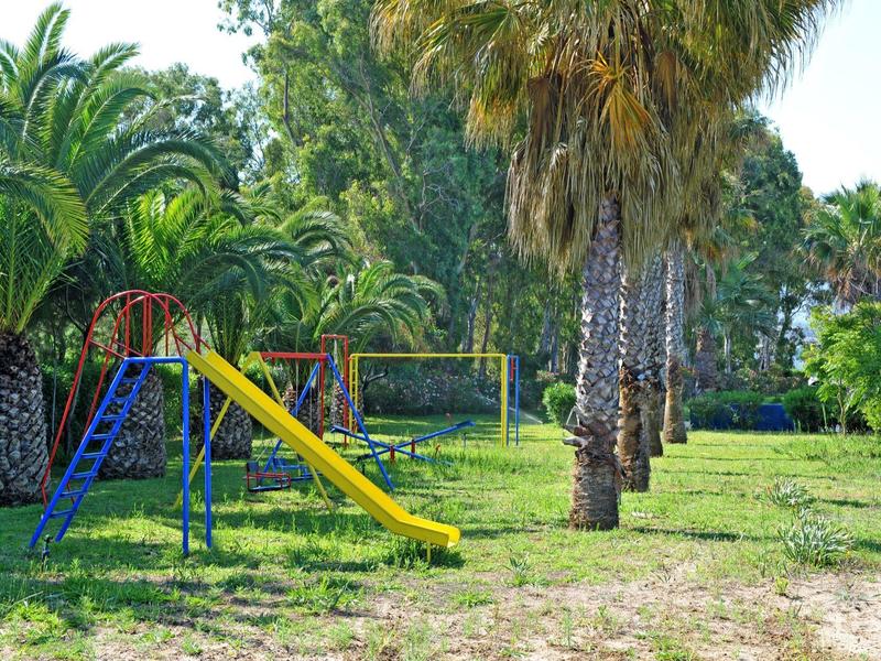 Plac zabaw dla dzieci z zjeżdżalnią i drabinką otoczony palmami w zielonym parku