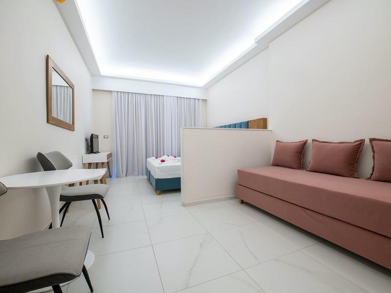 Nowoczesny pokój hotelowy z kanapą, łóżkami, krzesłami i biurkiem w jasnym stylu.