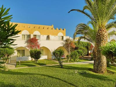Hotelanlage mit gelbem Dach, grüner Rasenfläche und Palmen unter blauem Himmel.