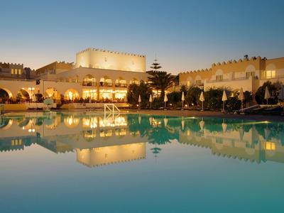 Luxuriöses Hotel mit beleuchtetem Pool bei Sonnenuntergang und klarer Spiegelung im Wasser.